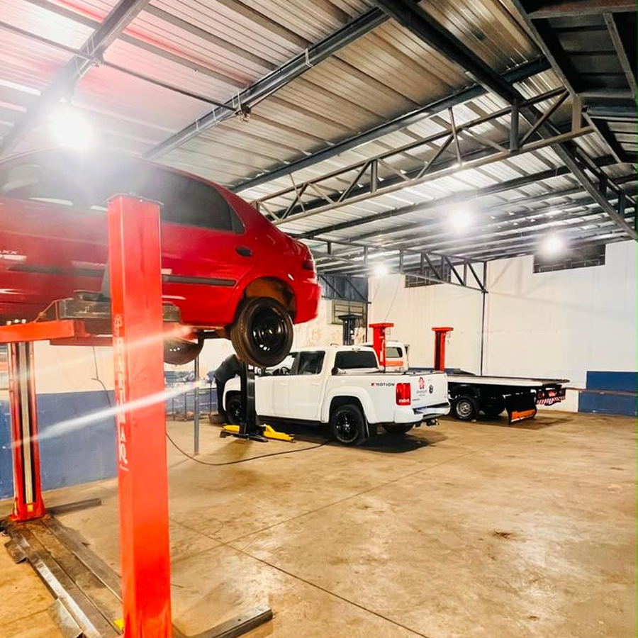 Hatch vermelho suspenso no elevador e picape branca no box da oficina da Mecânica ProAuto