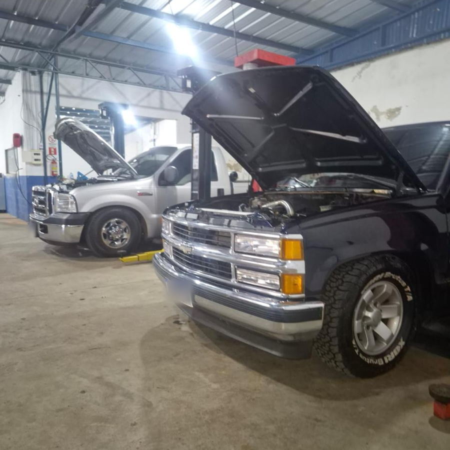 Ford F-250 prata e Chevrolet Silverado azul com os capôs abertos no galpão da Mecânica ProAuto em Ijuí